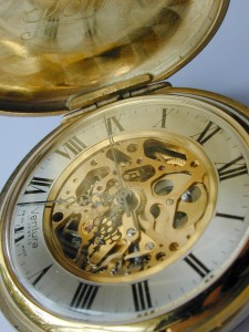 Dial and mechanism of an opened full hunter vintage pocket watch showing the cogs and wheels surrounded by the numerals